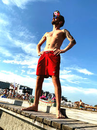 Full length of shirtless man standing against blue sky