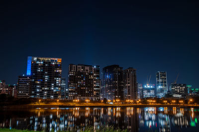Illuminated buildings by river against sky at night