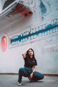 Portrait of young woman sitting against wall