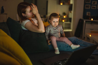 Side view of mother and daughter sitting on sofa at home