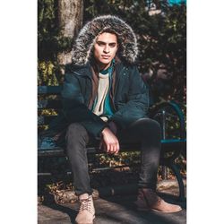 Portrait of young man wearing fur coat while sitting on bench at park