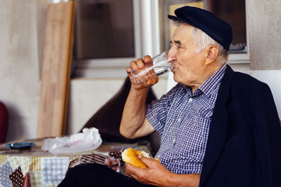 Senior man having food and drink while sitting on seat