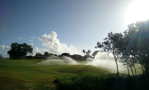 Irrigation sprinkler on golf course against sky on sunny day