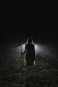 Ghost holding scythe standing in forest at night during rainy season