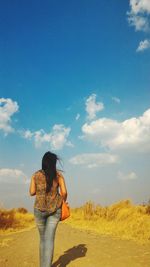 Rear view of woman walking on dirt road against sky