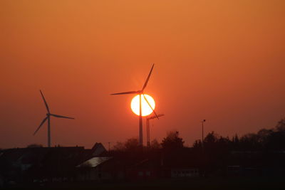 Silhouette of wind turbine against orange sky