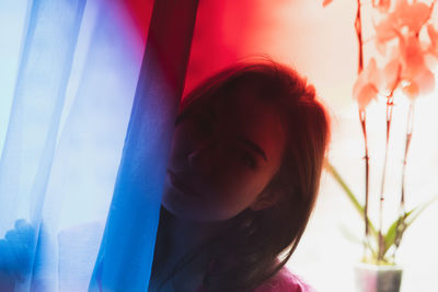 Close-up portrait of young woman with curtain on window at home