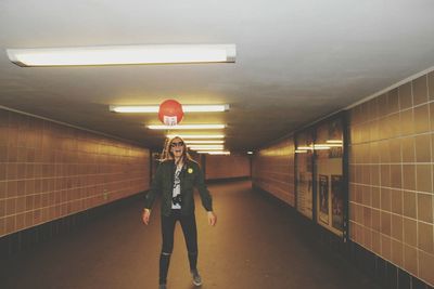 Full length of cheerful woman with helium balloon in illuminated tunnel