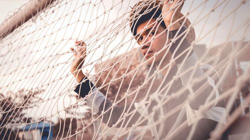 Portrait of young man looking through goal post during sunset