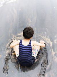 Rear view of boy sitting in water