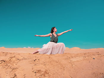 Woman with arms raised on beach against sky