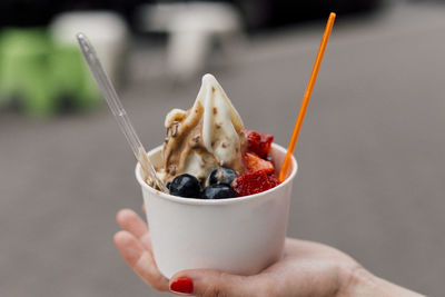 Close-up of female hand holding a cup of frozen yogurt with multiple toppings