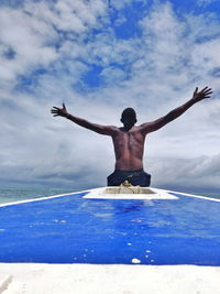 Rear view of shirtless man in swimming pool against sky