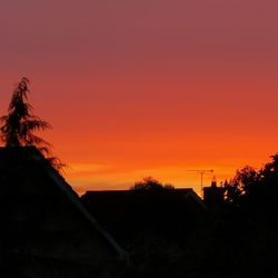 Silhouette tree and buildings against orange sky