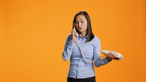 Portrait of young woman standing against yellow background