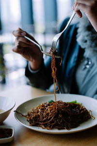 Cropped image of woman eating noodles at table