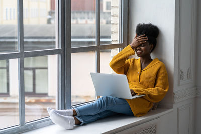 Young woman with laptop sitting by window at home