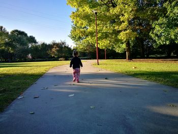 Rear view of child walking on footpath in park during sunny day