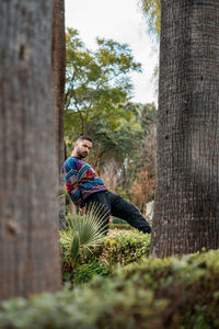 Caucasian model standing in between palm trees in a public park