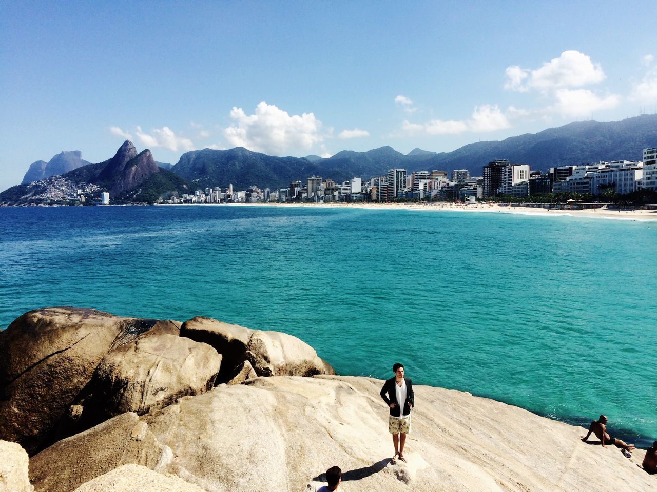 mountain, water, sky, building exterior, sea, architecture, leisure activity, mountain range, built structure, lifestyles, blue, full length, men, scenics, rear view, city, sitting, vacations