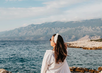 Rear view of young woman in white shirt standing on beach. sea, summer, view, lifestyle.