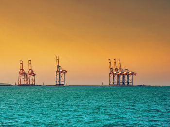 Cranes in sea against sky during sunset