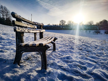 Snow covered bench on field against sky during winter