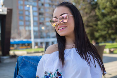 Happy young woman wearing sunglasses while sitting at outdoor cafe in city