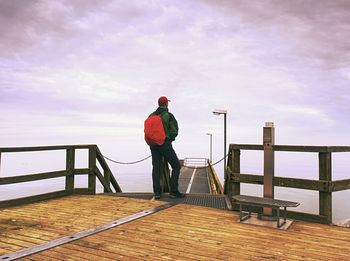 Rear view of man standing on railing against sky