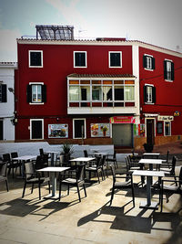 Empty chairs and tables at sidewalk cafe against buildings in city