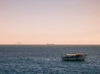 Boat sailing in sea against clear sky during sunset