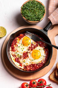 Flat lay image of shakshouka in a pan on a light coloured background close up