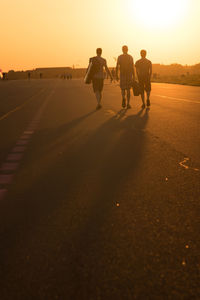 Rear view full length of friends walking on road against sky during sunset