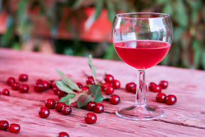 Rose cherry wine in glass stands wooden table with a bottle against a background of blurred greenery