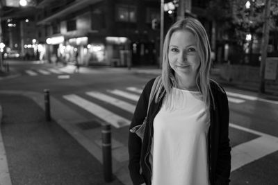 Portrait of smiling woman standing against road at night