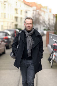 Portrait of man wearing winter coat while walking on footpath in city