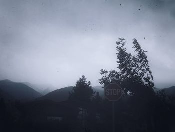 Road sign by trees against sky