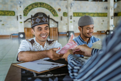 Smiling men receiving cash from person at mosque