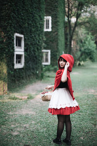 Full length portrait of woman standing by building at lawn