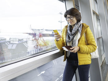 Smiling woman with passport ,boarding pass is texting on smartphone. tourist is waiting for boarding