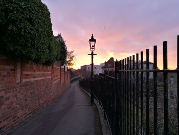 Walkway amidst trees against sky during sunset