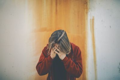 Man covering face while standing against wall