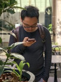 Young man using mobile phone in courtyard against reflective, glass windows and wall.