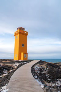 Lighthouse amidst sea and buildings against sky