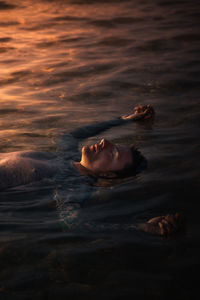 Man floating on water at sunset