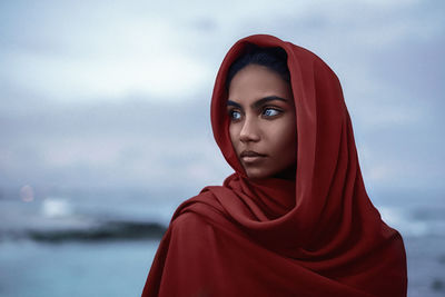 Portrait of young woman looking away against sky