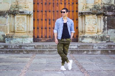 Full length portrait of young man standing against brick wall