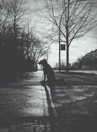 Silhouette boy walking on road by bare trees