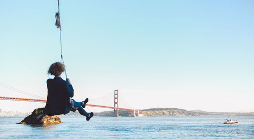 Rear view of woman sitting on swing with golden gate bridge in background