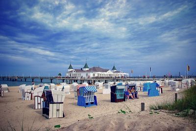 Hooded chairs at beach by house on pier against sky